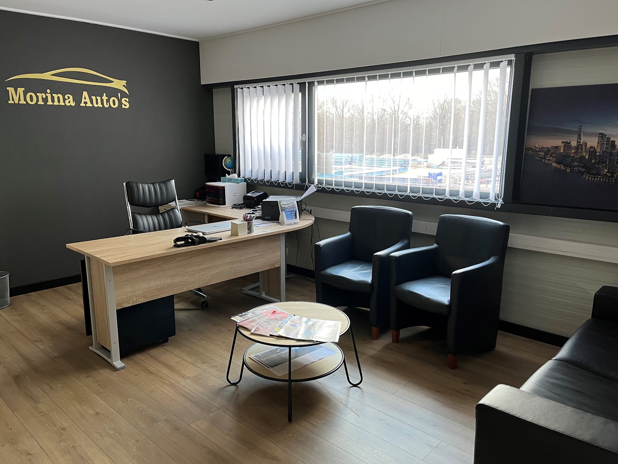 De ontvangstruimte van Morina Auto's, met het logo op de wand en twee fauteuils